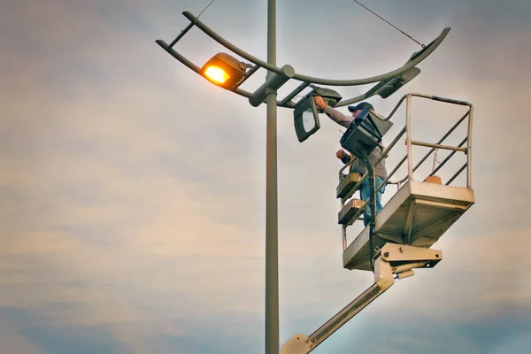 Réparation professionnelle et entretien des lampadaires - grue a soulevé un électricien pour remplacer les ampoules au coucher du soleil dans la soirée. Tonique dans les filtres de style instagram. Espace de copie vide pour le texte . Images De Stock Libres De Droits