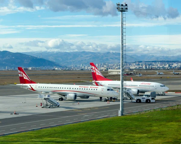 İki Gürcü uçak Airzena airways airport adlı park ettiniz. Arka plan güzel manzara - şehir gökdelenler, dağlar ve bulutlar ile gökyüzü.