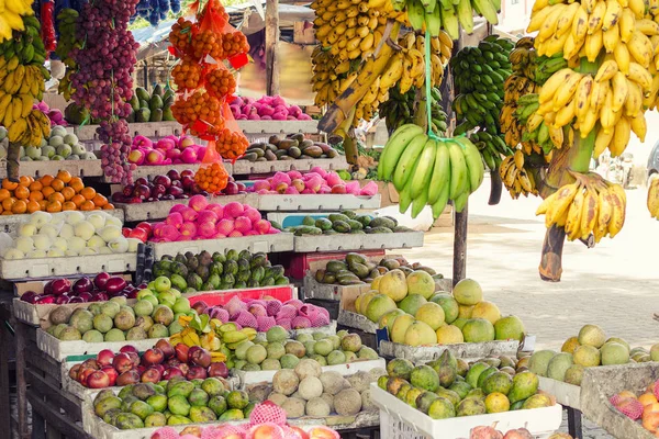 Fruit store on Sri Lanka Street with variety of exotic fruits in boxes and bunches of bananas on branches. Agricultural products on market in Asia.