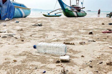 Boş kullanılan plastik şişe kapatın ve arka plan üzerinde deniz sahilde atılmış diğer atık balıkçı tekneleri.