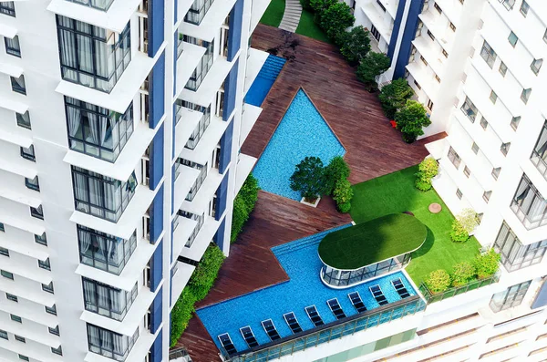 Details of modern building exterior - patio in high-rise building with swimimg pool, lounge zone, green trees. Everything for comfortable stay, ideal exotic vacation.