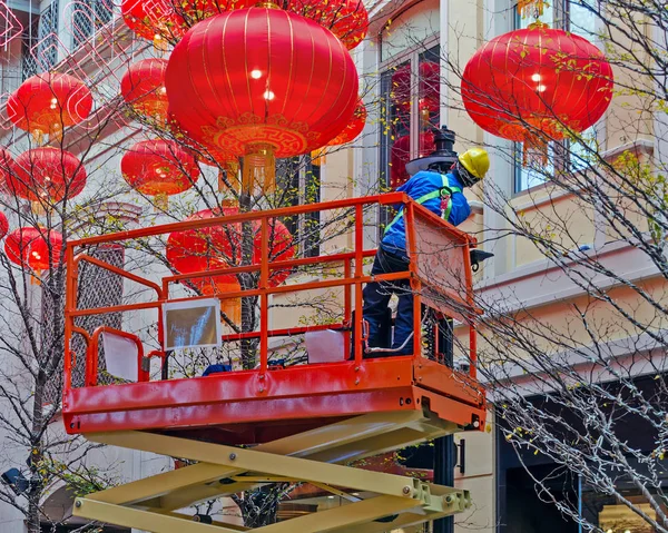 Electrician on a hydraulic scissor lift is serving a street lamp. Around the decoration of Chinese lanterns