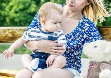Dizlerinin üzerinde bir oyuncak ayı bir parkta bir bankta oturuyor küçük oğlu olan genç mather