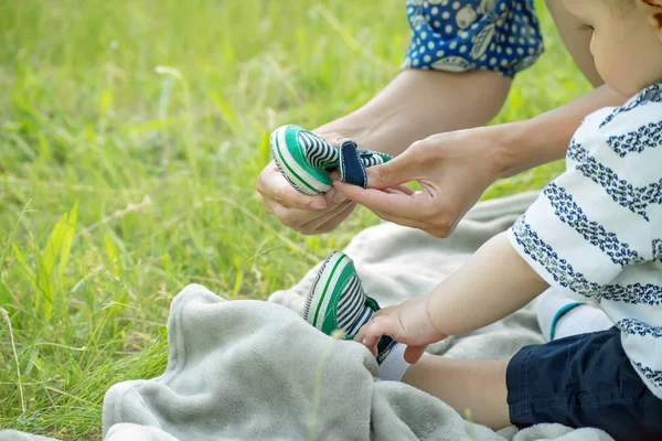 Mãos carinhosas de uma jovem mãe vestindo uma criança em um parque de verão na grama — Fotografia de Stock