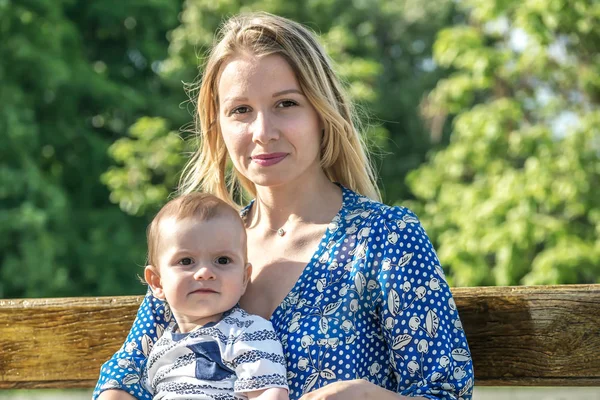 Küçük bebek oğlu bir bankta açık olan bir genç güzel motherr