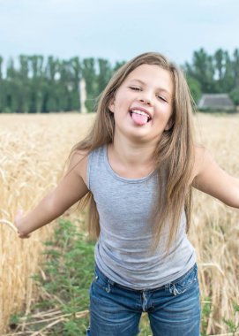 playful little girl showing her tongue in wheat field at a summer day clipart