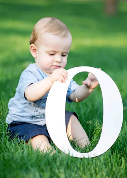 Babyjongen spelen met grote witte letter O zittend op groen gras op zomerdag — Stockfoto