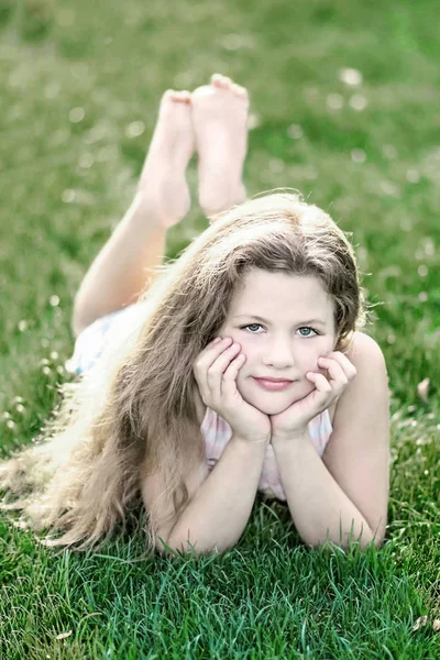 Little beautiful girl with long loose hair on green grass at summer day — Stock Photo, Image