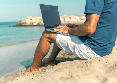 Deniz kıyısında otururken dizüstü bilgisayarda çalışan yetişkin biri. Mesafeli iş. Telework.
