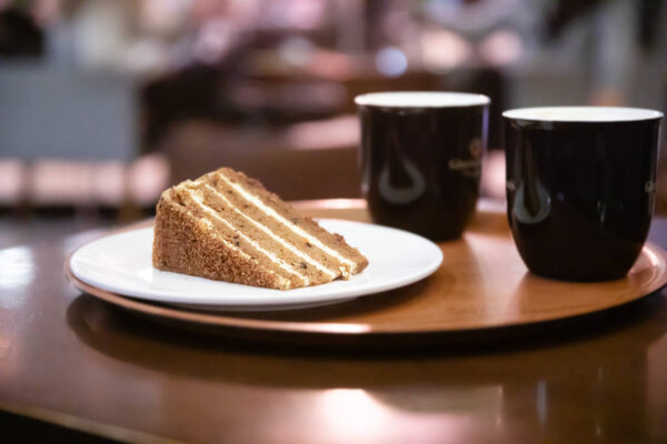 Two Coffee cups and a plate with carrot cake or pie on a on a round tray on a table in a cafe in evening or at night