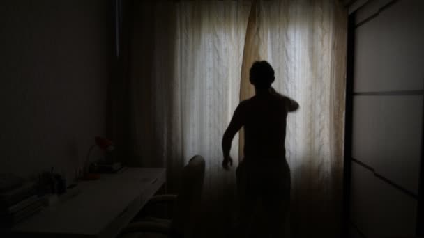 Homem com uma luz de fundo abre as cortinas em uma manhã ensolarada — Vídeo de Stock