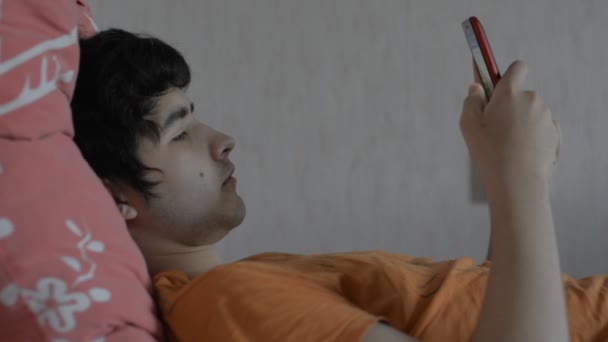 Молодой мужчина со смартфоном, лежащим на кровати — стоковое видео