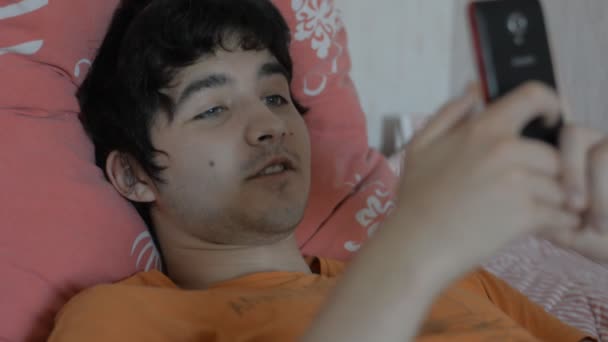Молодой человек со смартфоном, лежащим на кровати — стоковое видео