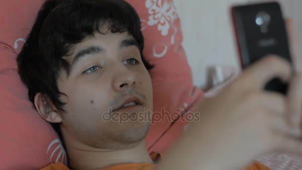 Young man with a smartphone lying on the bed — Stock Video