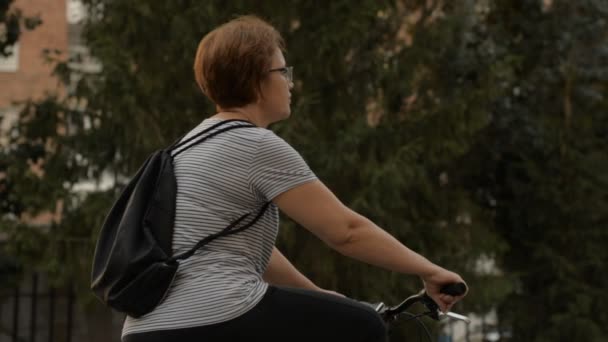 Женщина в очках начинает на велосипеде в парке — стоковое видео
