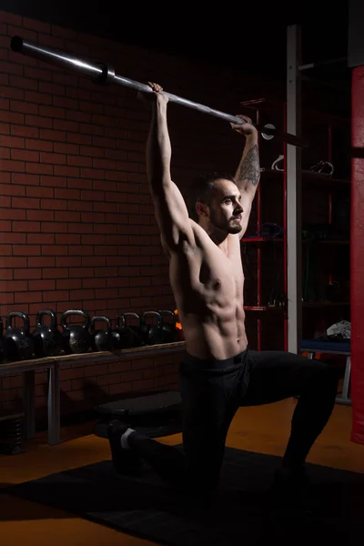 Junger muskulöser Mann mit Langhantelstange im Fitnessstudio — Stockfoto