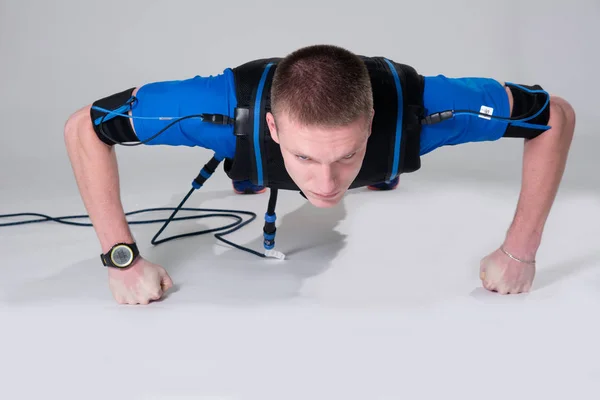 Man in an electric muscular suit for stimulation does push-ups on the fists — Stock Photo, Image