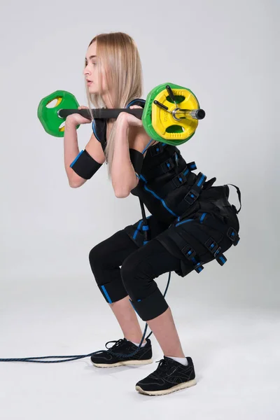 Belle blonde dans un costume musculaire électrique pour stimuler les exercices avec un haltère — Photo