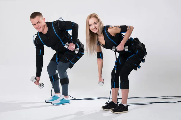 Young man and woman in electric muscular suit for stimulation with dumbbells — Stock Photo, Image