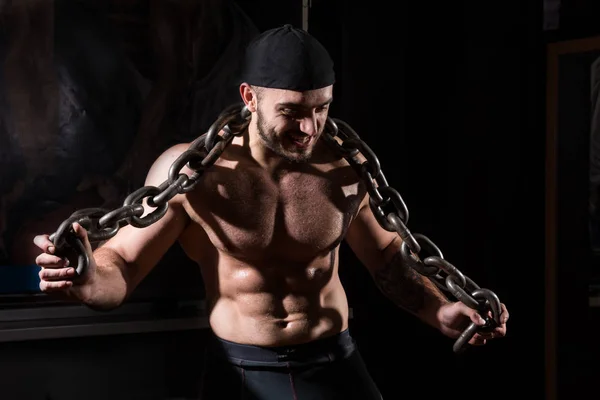 Молодой мускулистый мужчина с цепями в спортзале — стоковое фото