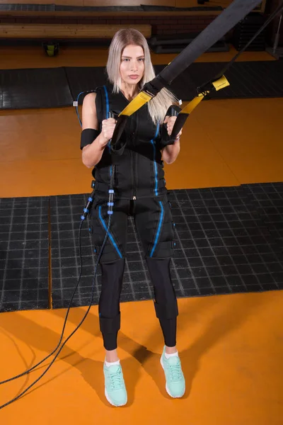 Belle femme en costume de stimulation musculaire électrique faisant de l'exercice squat pour le dos et avec suspension — Photo