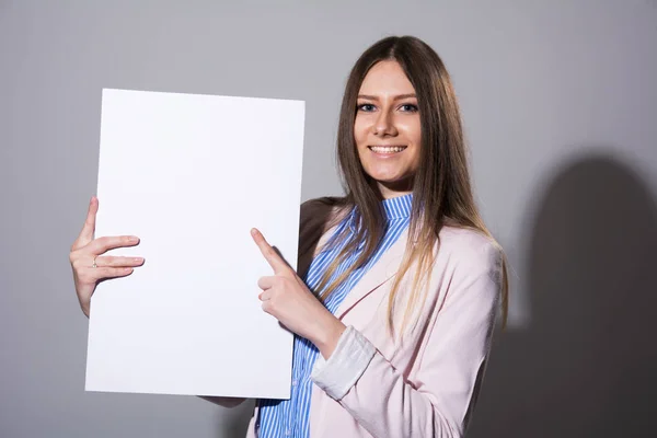 Jonge lachende vrouw wijst op een leeg wit vel — Stockfoto