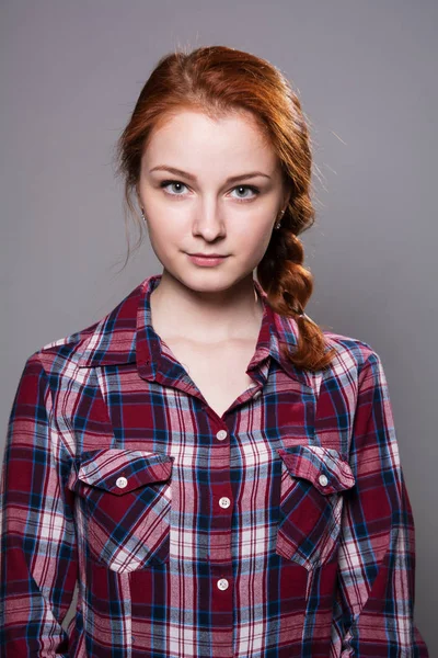 Portréja egy fiatal vörös hajú lány egy kockás inget, egy szürke háttér — Stock Fotó