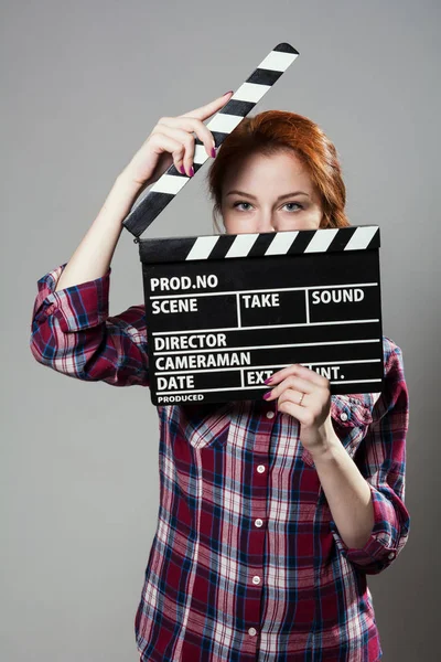 Schöne rothaarige Frau hält einen Filmklöppel in der Hand, isoliert über grauem Hintergrund. — Stockfoto