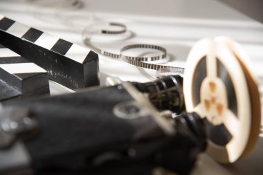 Eski bir film kamerası ve el çırpma makinesinin arka planına karşı bir ışık makarasında sarılı olmayan dar bir retro film. Sinema film aksesuarları