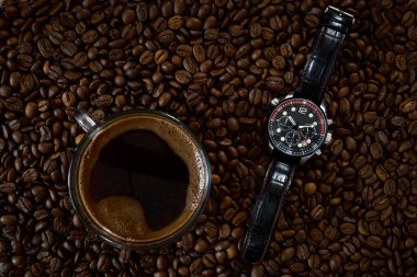 Kahve çekirdeğinin arka planında erkek saati olan bir fincan kahve.