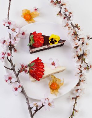 Çiçekli meyve dalları ve beyaz bir tabağa dizilmiş iki dilim pasta.