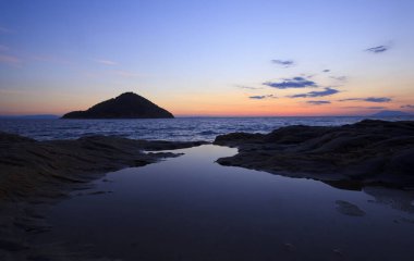 Yunanistan 'ın Thassos adasında sabah deniz manzarası. Ön planda sakin bir deniz ve ufukta yalnız bir adanın arkasında yükselen bir güneş..