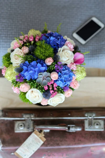 Flores mezcladas en la caja cerca de la cama con teléfono y maleta —  Fotos de Stock