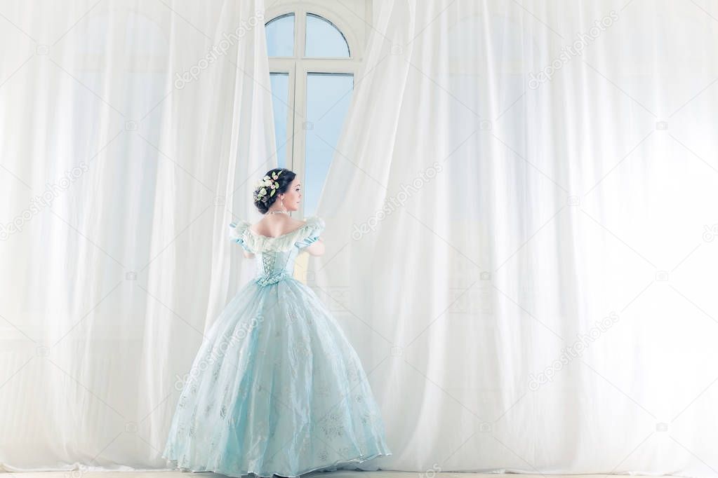 Elegant woman at a high window in historic dress, straightens the curtains, and waiting for friends to prom to dance