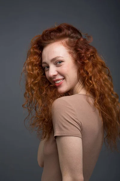 Happy curly red-haired woman with a beautiful smile. On an isolated gray background. The concept of happiness and emotions