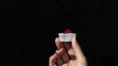 Siyah manikürlü güzel bir kadının elleri siyah arka planda beyaz bir ambalajda kırmızı el yapımı şekerler gösteriyor.