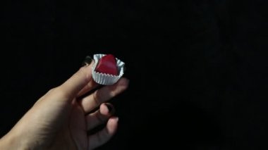 Siyah manikürlü güzel bir kadının elleri siyah arka planda beyaz bir ambalajda kırmızı el yapımı şekerler gösteriyor.