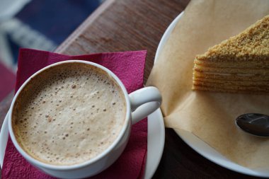 Kahvaltı, bir fincan cappuccino ve bir dilim ballı kek küçük kaşıkla beyaz bir fincan üzerinde