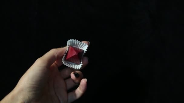 一个年轻女子的美丽的手在运动中的黑色指甲显示红色手工制作的糖果 白色包装 黑色背景 — 图库视频影像