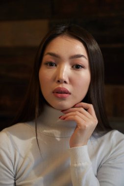 Yakalı genç bir Asyalı kızın portresi balıkçı yaka kazağından yüzüne doğru döndü, doğrudan kameraya baktı, bir kazakla. Cilt bakımı ve saç konsepti                                 