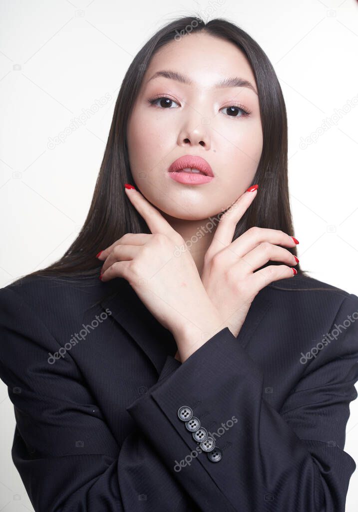  Portrait of a young beautiful Asian girl holding her hands to her face, looking directly at the camera, wearing a blue jacket. The concept of skin care and hair                               