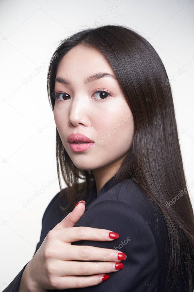 Portrait of a young Asian girl, standing sideways to the camera , holding her hands at her shoulder , looking directly into the camera, wearing a blue jacket. The concept of care of skin and hair                               