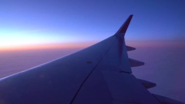 Pencereden uçağın kanatlarını görebilirsiniz, bulutların arka planına karşı havada, arka planda, uçak uçuyor. Kanatta seyir ışıkları yanıp sönüyor. Uçakla yolculuk, bir gecelik uçuş.