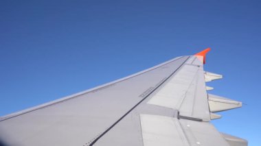 Pencere deliğinden uçağın kanadının parlak mavi gökyüzüne karşı nasıl havada olduğunu görebilirsiniz, uçak döner ve yana yatar, sonra zemini görebilirsiniz. Gün boyu uçakla yolculuk, güzel mavi gökyüzü