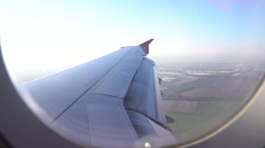 Pencereden uçağın kanadını görebilirsiniz, uçak iniyor, arka planda şehri görebilirsiniz, bulutları. Uçakla yolculuk, gündüz uçuşu.