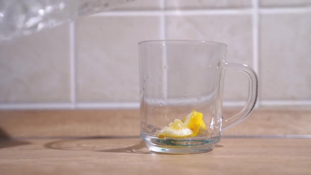木製のテーブルの背景には透明なガラスがあり 女性の手はそれにレモンキューブを入れ ガラスのカフェから水を注ぎます スローモーション — ストック動画