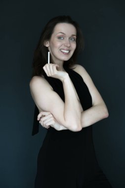 Uzun saçlı genç bir kadının portresi, başka tarafa bakıyor, gülümsüyor, elinde sigara tutuyor, gri bir arka planda.