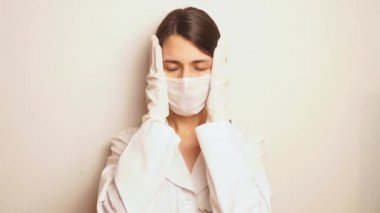 Güzel bir kadın doktor izleyiciye ciddi şekilde bakar, derin bir nefes alır, üniforma giyer, koruyucu bir maske takar ve tek kullanımlık eldivenler giyer, hasta sayısından, endişelerden, bir sürü işten başını alır.