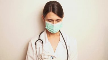 Mavi maskeli ve tek kullanımlık eldivenli bir kadın doktor tek kullanımlık şırıngayı çıkarır ve ellerini dezenfekte eder.)