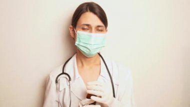 Maske takan ve tek kullanımlık eldiven takan bir kadın doktor ellerinde dezenfektan, ellerini dezenfekte etmesi ve kendini koruması için bir hatırlatma olarak tutuyor.